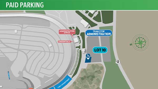 Map graphic titled “Paid Parking” showing a section of Michigan International Speedway near the administration area. The racetrack and surrounding roads are displayed in gray on the left side. A blue label marks the “Administration” tram stop beside Lot 10, which is highlighted in blue near Highway 12 on the right side of the map. Additional labels identify the Administration Office, Credentials, and Turn 1 Credentials areas. A wheelchair accessibility icon appears next to Lot 10. A compass rose is shown in the upper-right corner.